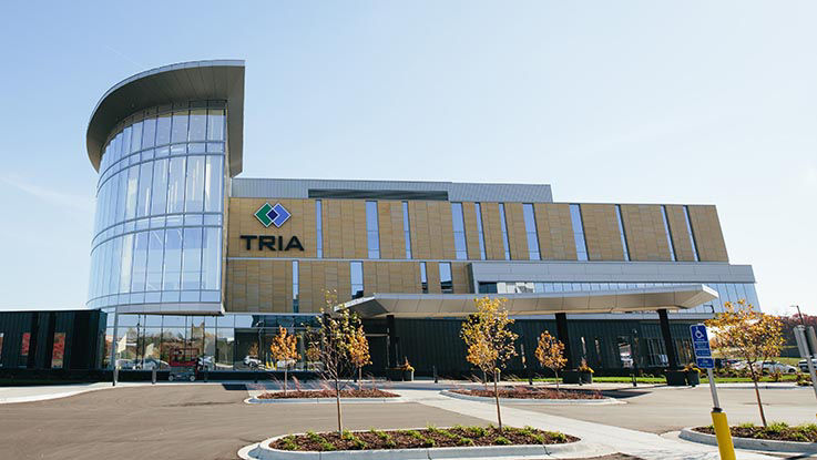 A picture of the entrance to TRIA Woodbury. It’s a modern building with several windows and ample parking.