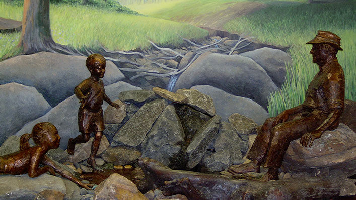 Statues of a father and two children are placed in front of a woodland mural.