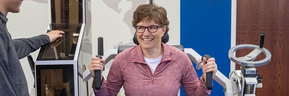 A patient smiles as she exercises on equipment designed to target the muscles in the neck and back.