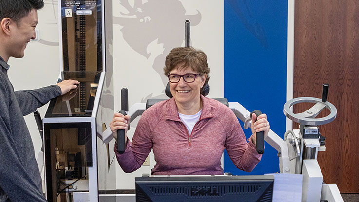 A patient smiles as she exercises on equipment designed to target the muscles in the neck and back.