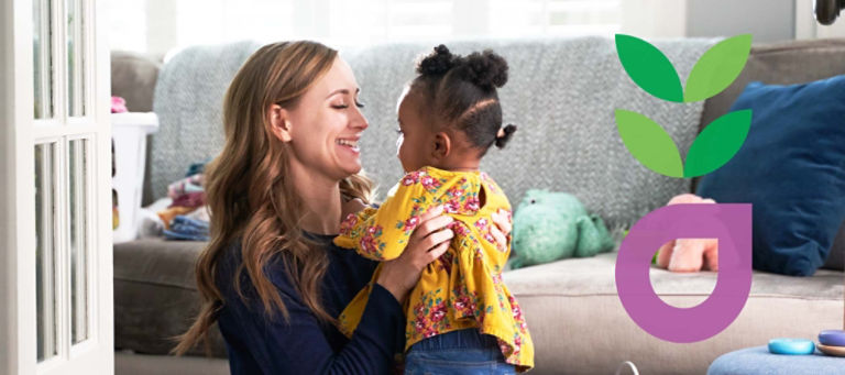 A white mom is holding her biracial daughter and smiling.