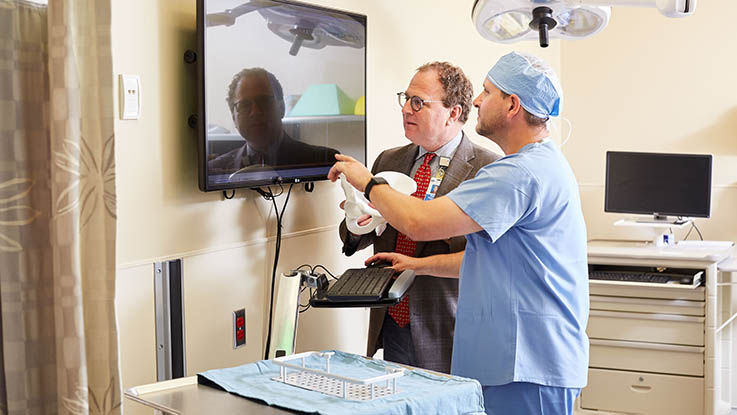 A surgeon shows his colleague patient details on a computer in an exam room.