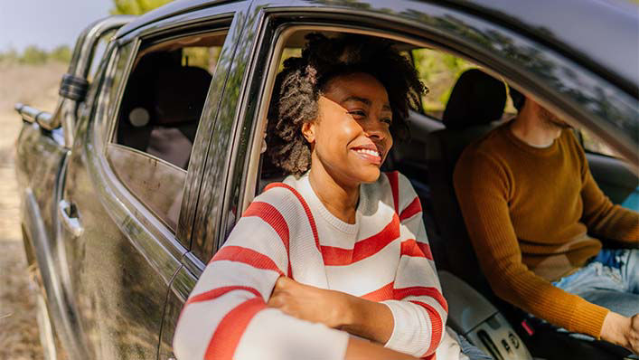 Riding in the passenger seat of a truck while her husband drives, a smiling woman rests her arm outside an open window.