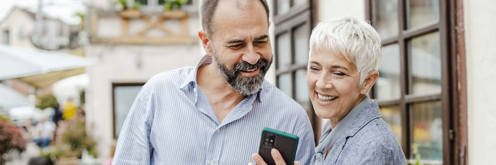 An older man and older woman smile as they look at information on a smartphone