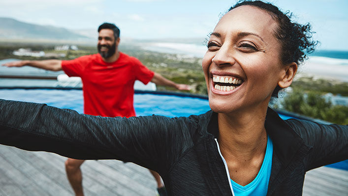 A man and woman smile as they practice yoga on a rooftop.