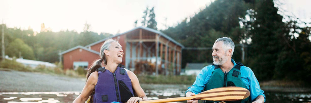 A man and woman laugh together as they canoe across a rural lake