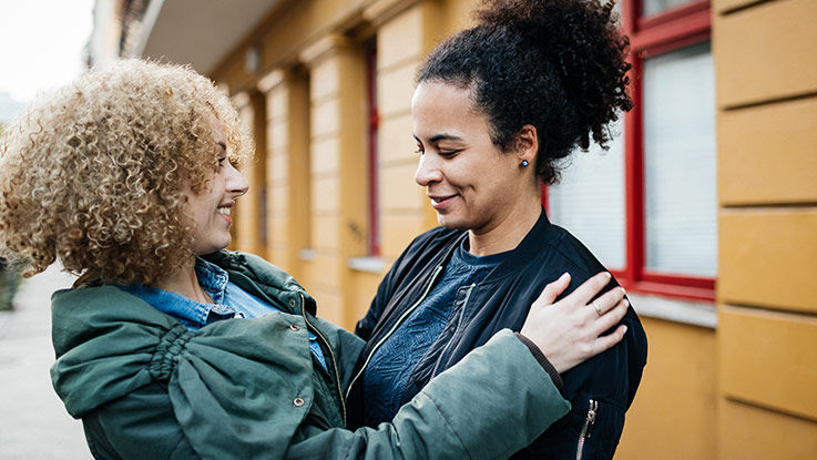 Two women embrace outside on a cloudy day.