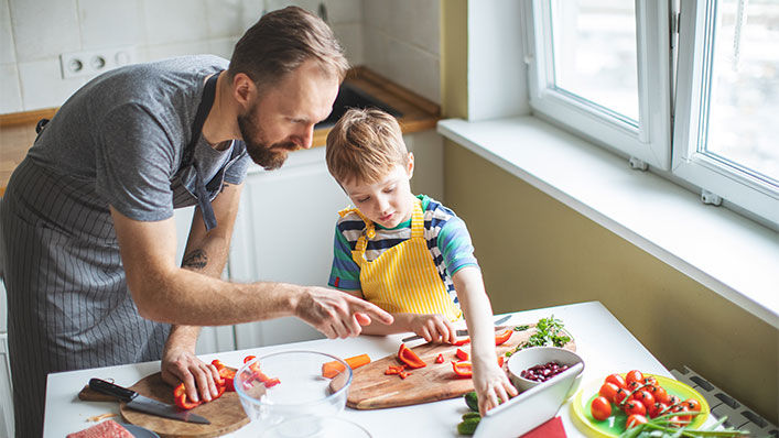 A father and son work together to chop up many different vegetables for dinner.