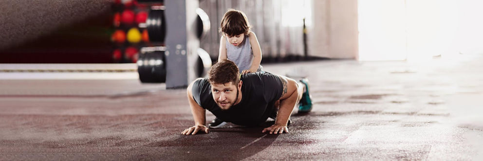 A father does a push-up at the gym with his young son on his back.