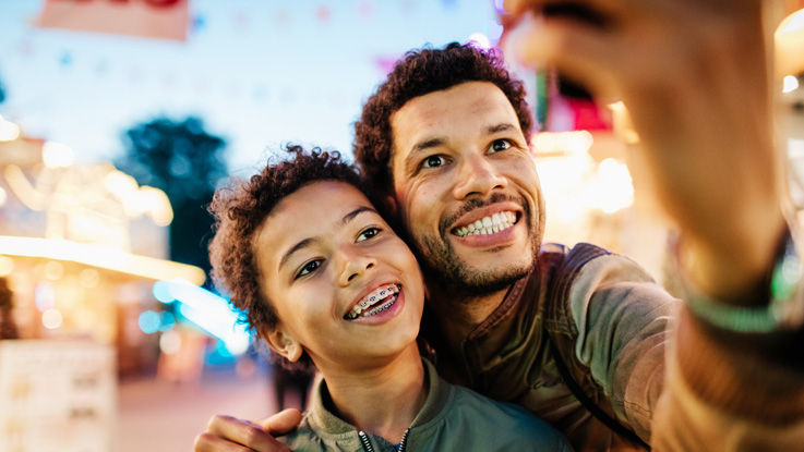 A smiling father and son take a selfie at an amusement park.