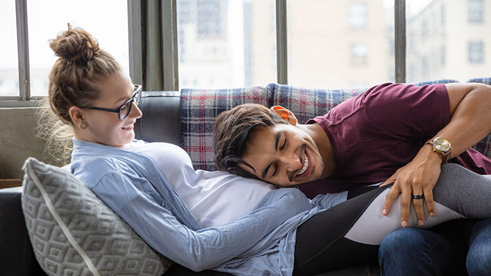 A man lays his head on his pregnant wife's belly as she reclines on the couch.