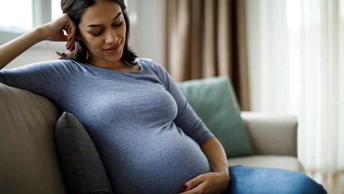 A pregnant woman relaxes on the couch with a hand on her belly. 