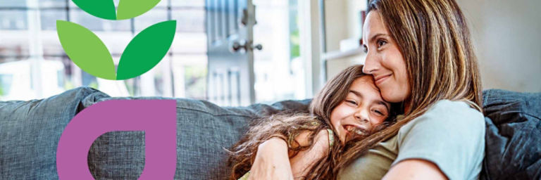 A mom and her tween daughter happily snuggle on the couch.