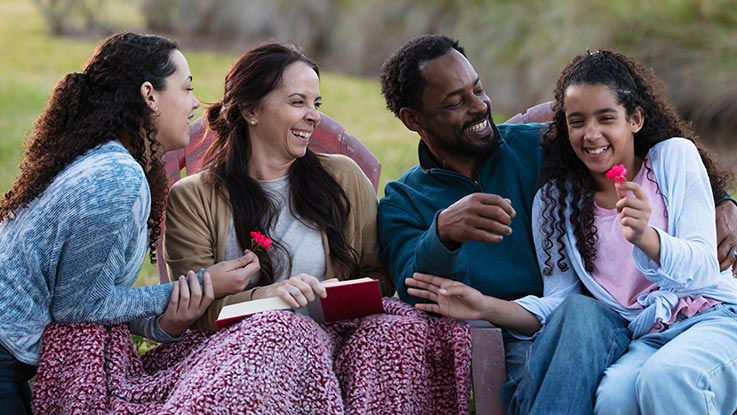 A man, a woman and their children laugh as they sit together in a field sharing stories