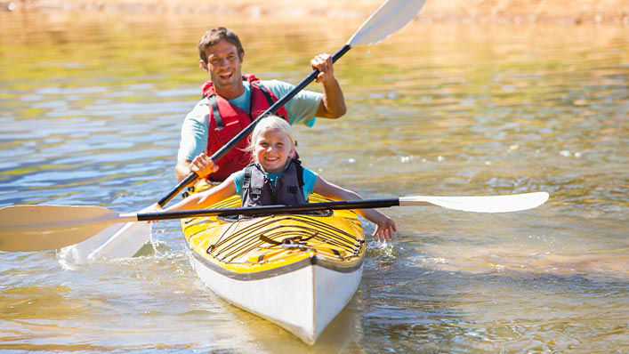 Father and daughter kayak together on a local lake. 