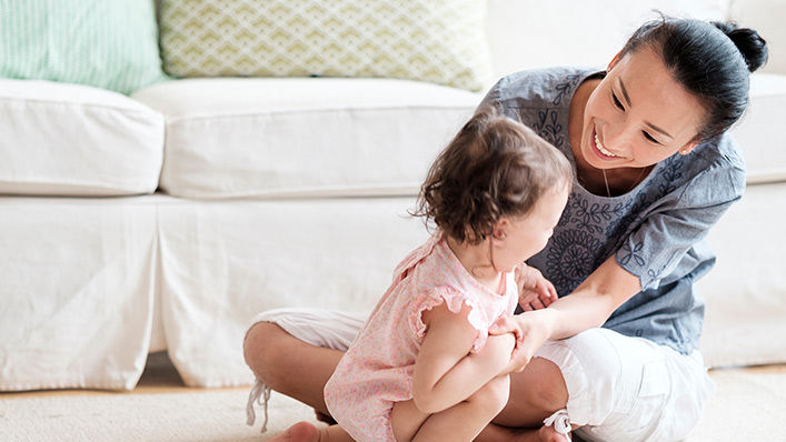 Mother playing with newborn baby girl in living room