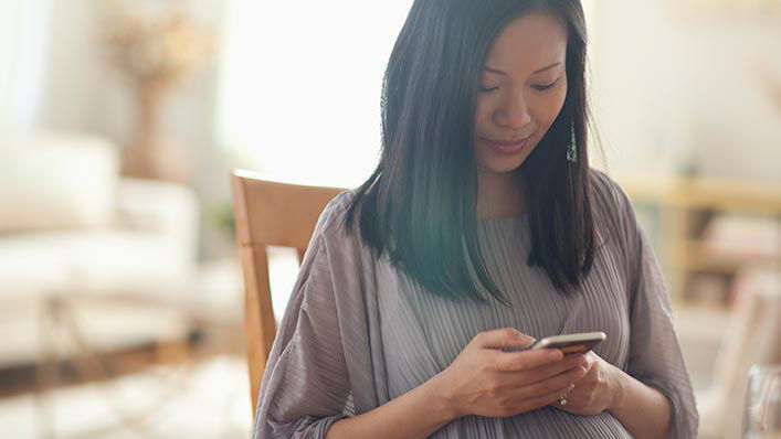 A pregnant woman relaxing at home looks down at her phone.