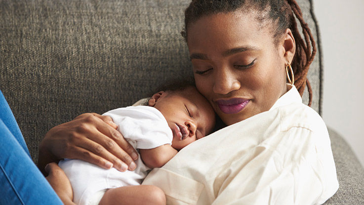 A mother relaxes on a couch with her baby in her arms.