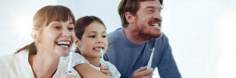 A couple and their daughter brush their teeth together in front of a mirror