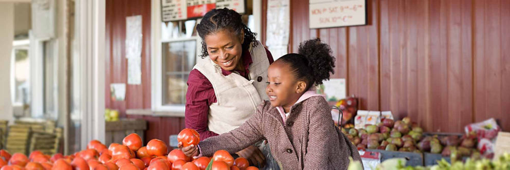 An older woman picks out produce at a grocery store with her granddaughter.