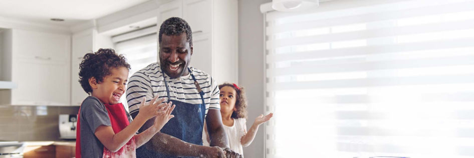 In a kitchen, a father and his two young children laugh and have fun cooking a meal together