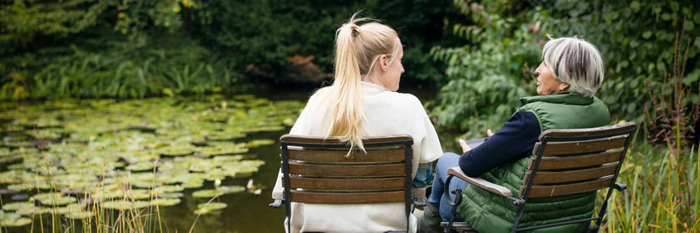 A woman sits with her grandmother next to a peaceful pond.