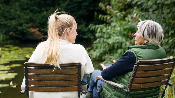 A woman sits with her grandmother next to a peaceful pond.