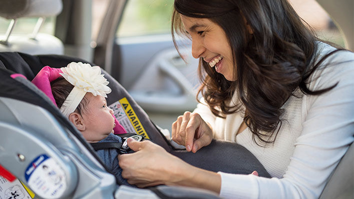 A mom buckles her newborn baby into a car seat.