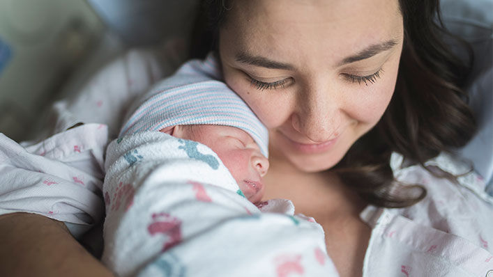 A mom snuggles with her newborn baby in bed.