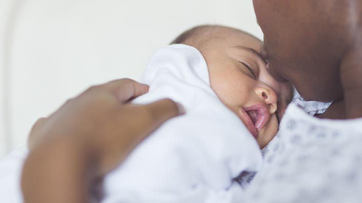 A mother kisses her newborn baby on the forehead.