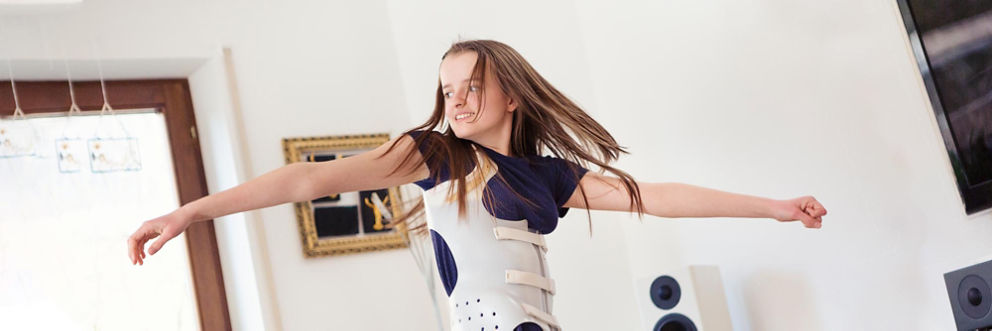 A preteen girl wearing a back brace dances in the living room.