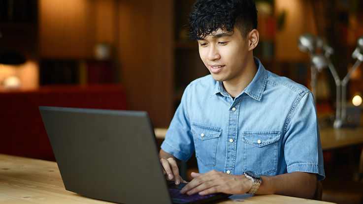 A teen boy uses his laptop at a table