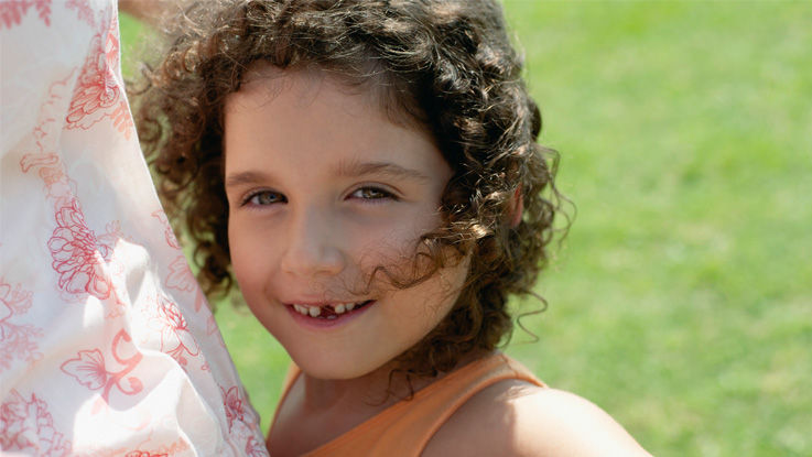 A curly-haired boy with a missing front tooth grins in the sunshine.