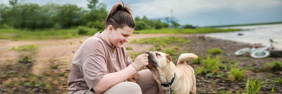 A teenager plays with her dog alongside a scenic lakeshore