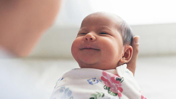 A newborn baby smiles up at his mother.