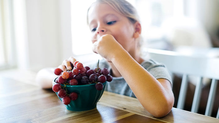 A young girl eats from a bowl of grapes.