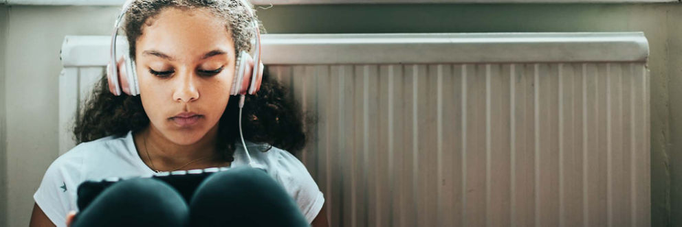 A teenage girl wearing headphones looks at something on a tablet.