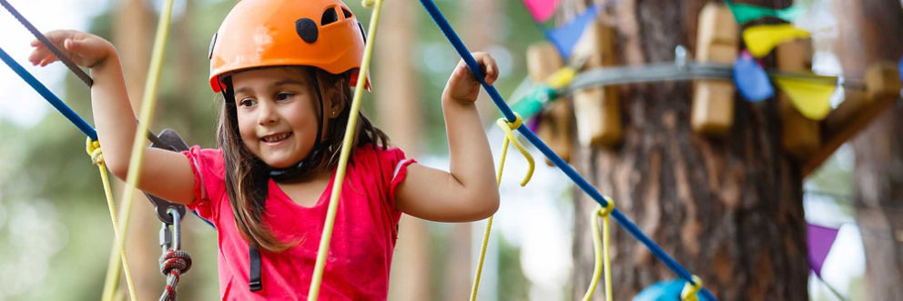 A smiling young girl wearing a helmet walks along a ropes course.