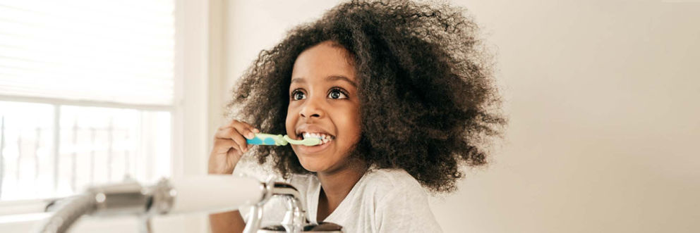 A young girl eagerly brushes her teeth as she stands in front of a bathroom sink.