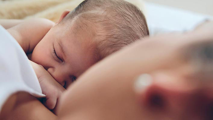 A mom snuggles with her newborn baby in bed.