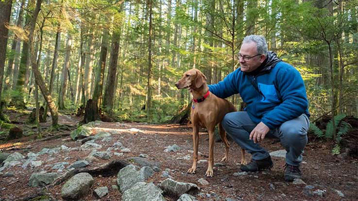 An older man pauses with his dog during a walk in the woods on a nice sunny day
