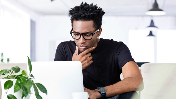 Sitting in a conference room, a young man looks intently at his laptop.