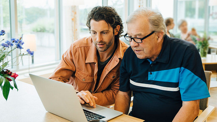 A father and adult look at information on a laptop.