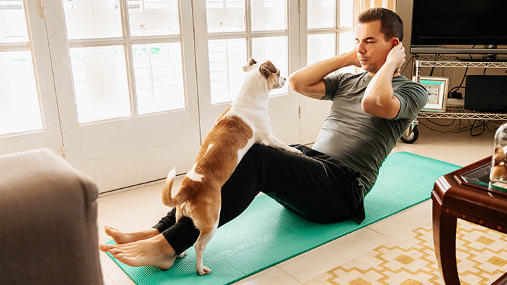 A man attempts to do yoga while his dog leans against him, wanting attention.