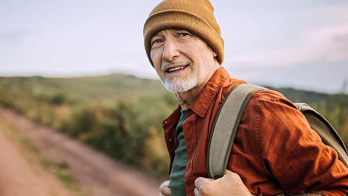 An older man in the countryside looks back briefly as he prepares to begin a hike