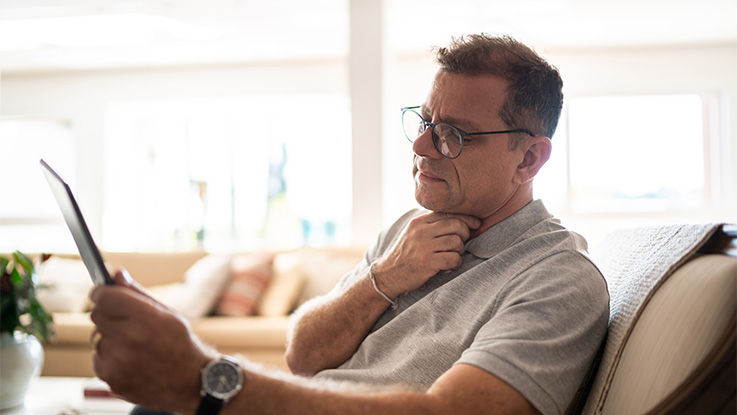 A man motions to his throat while describing his symptoms to his doctor during a video visit.