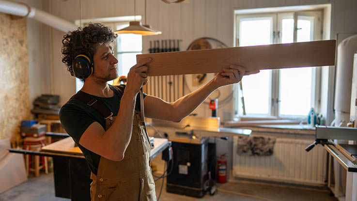 A carpenter working in his workshop measures a piece of wood