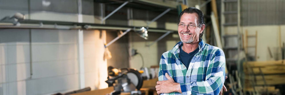 An older man smiles as he stands in his tool shop