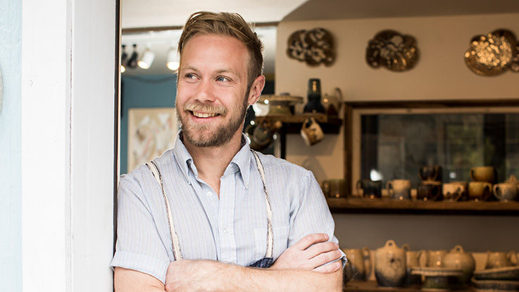 A smiling young antiques shop owner stands in the doorway of his business.