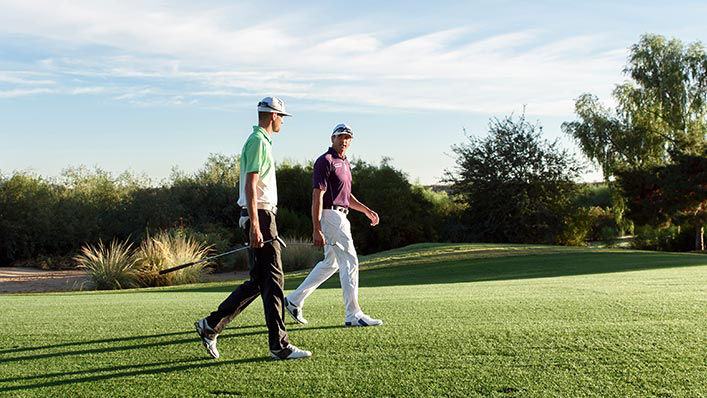 Two male golfers walk and talk during a golf tournament.